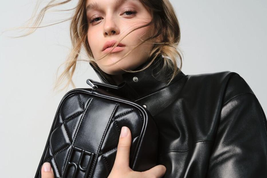 Eine Frau mit Lederjacke hält eine schwarze, gesteppte Handtasche.