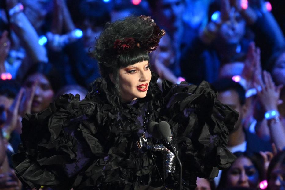 Eine Sängerin in einem extravaganten schwarzen Kleid steht auf einer Bühne vor Publikum.