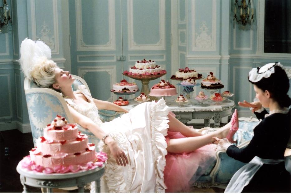 Eine Frau im Rokoko-Kleid ruht sich aus, während ein Dienstmädchen ihr die Schuhe anzieht, umgeben von Kuchen.