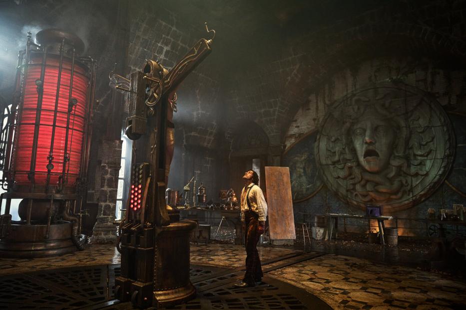 Filmszene: Victor Frankenstein steht in seinem Labor und sieht auf seine Kreatur, die auf einem Kreuz aufgepannt ist.