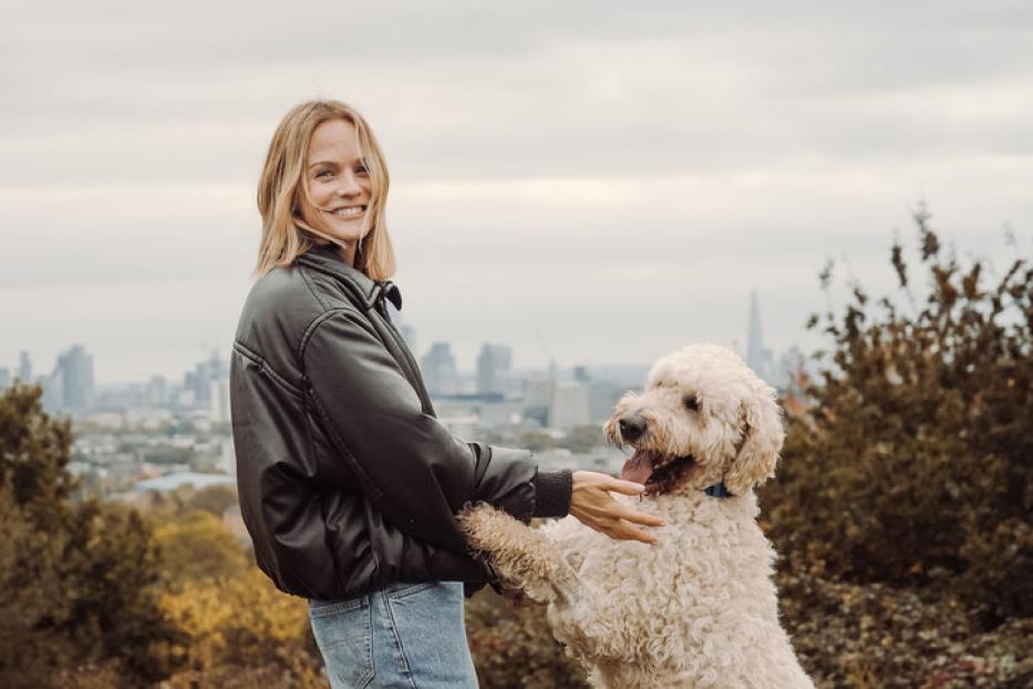 Ein beiger, wuscheliger Hund, wie er mit Moderatorin Mirjam Weichselbraun auf einer Wiese spielt