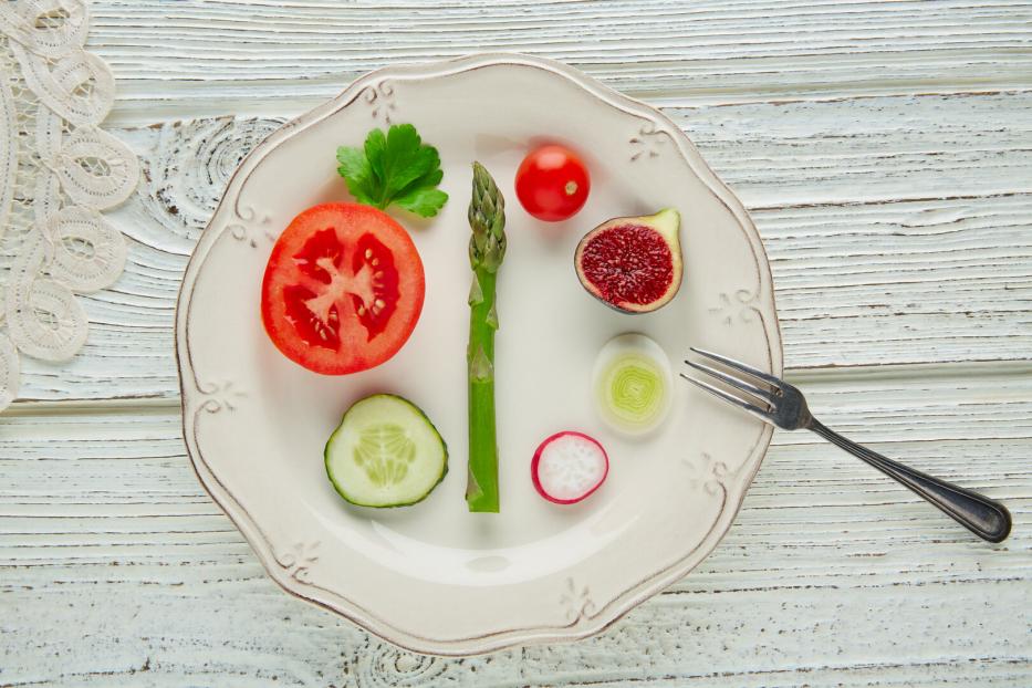 Verschiedene Gemüsescheiben, eine Feige und ein Spargel liegen dekorativ auf einem weißen Teller mit einer kleinen Gabel.