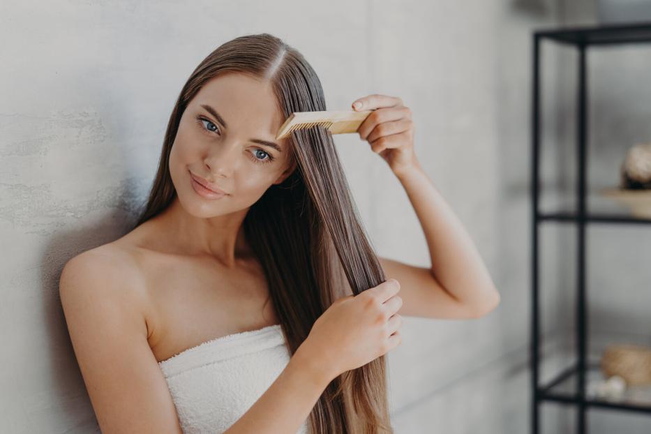 Eine junge Frau mit einem Handtuch um den Körper kämmt ihr langes, braunes Haar.