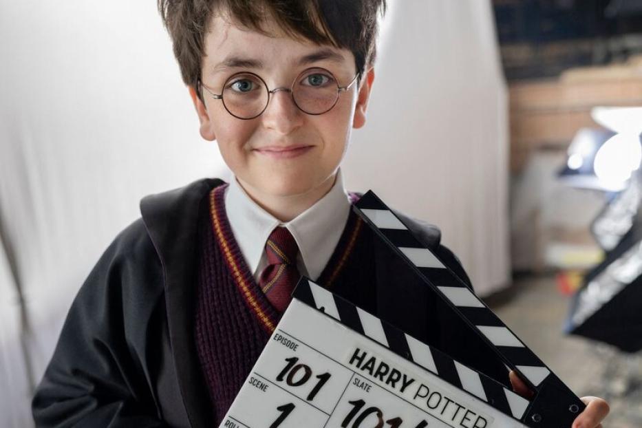 Ein junger Schauspieler im Harry-Potter-Kostüm hält eine Filmklappe mit der Aufschrift "Harry Potter, Episode 101".