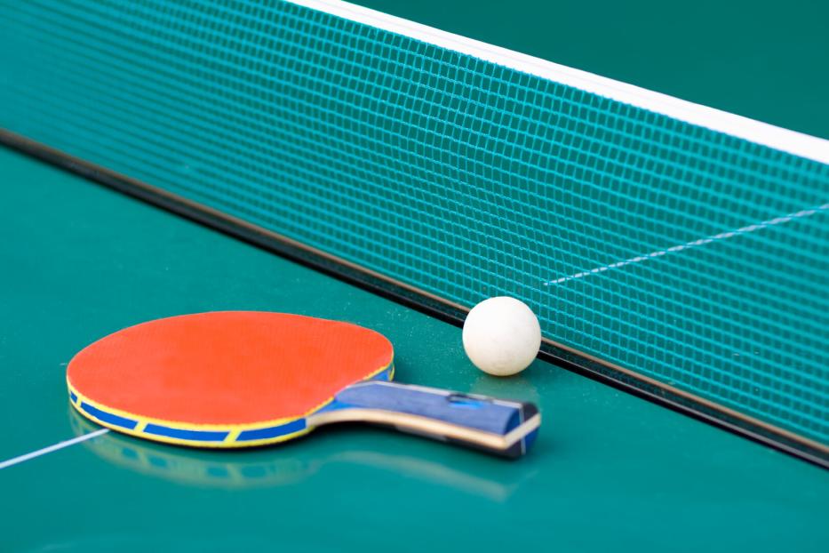 Tischtennisschläger und Ball liegen vor dem Netz auf grünem Tisch.
