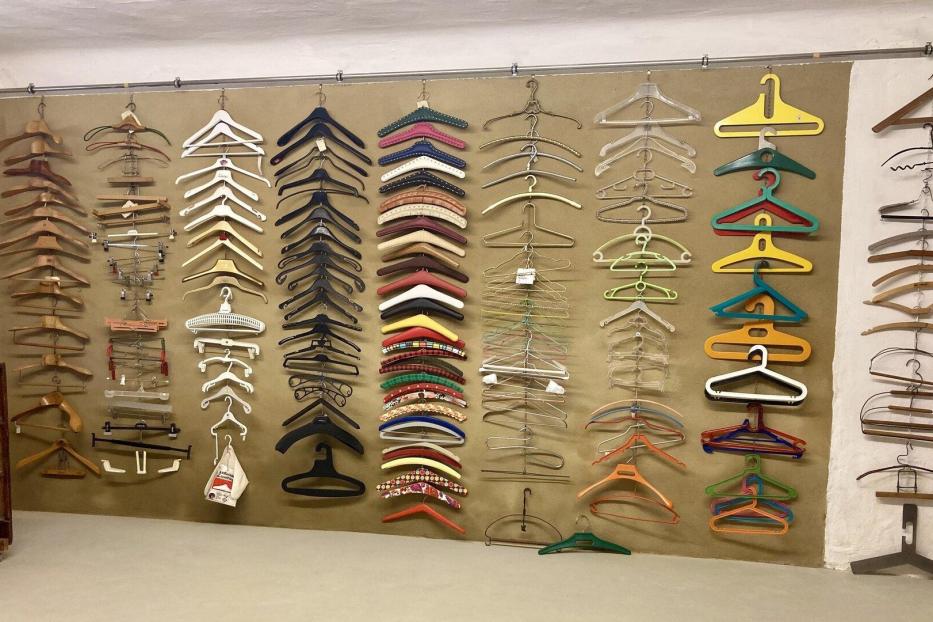 Viele verschiedene Kleiderbügel aus Holz, Kunststoff und Metall sind ordentlich an einer Wand angeordnet.