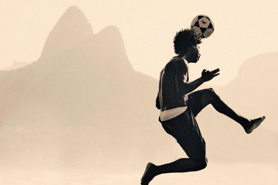 Ein junger Mann jongliert vor der Silhouette des Zuckerhuts in Rio de Janeiro einen Fußball mit dem Kopf.