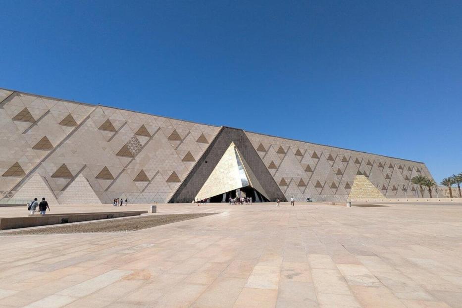 Die Fassade des Grand Egyptian Museum in Gizeh mit ihrem markanten dreieckigen Eingang vor einem klaren blauen Himmel.