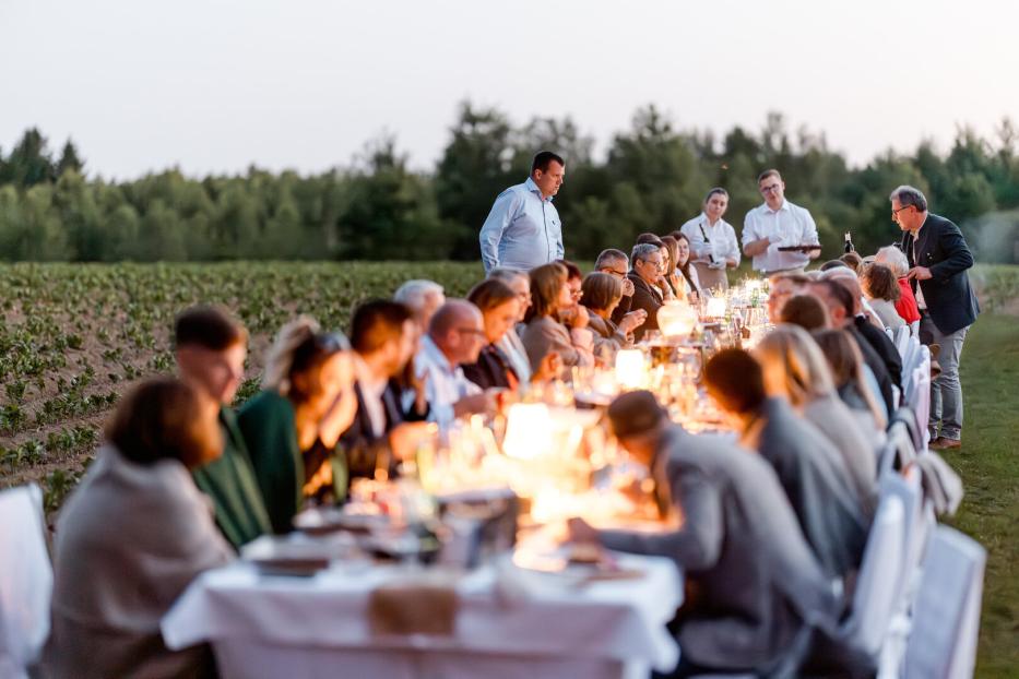 Lange Tafel mit Gästen und Kerzenlicht im Freien zwischen Feldern bei einer Abendveranstaltung der Waldviertler Tischkultur 2025.