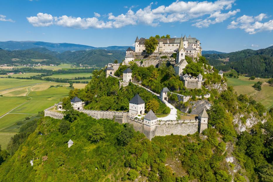 Die Burg Hochosterwitz thront auf einem bewaldeten Felskegel inmitten einer grünen Hügellandschaft in Kärnten.