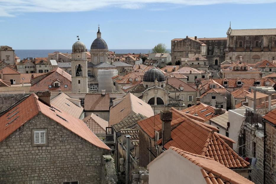 Blick über die Altstadt von Dubrovnik mit ihren charakteristischen roten Ziegeldächern und historischen Steingebäuden vor dem blauen Meer.