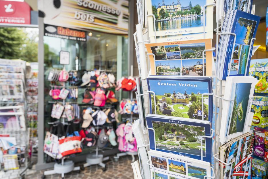 Postkartenständer vor einem Souvenirshop mit Ansichten vom Wörthersee und Schloss Velden.