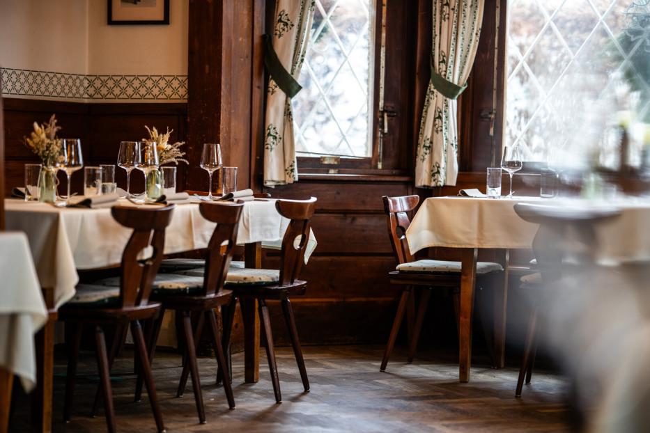 Gemütliches Restaurant mit gedeckten Tischen, Holzstühlen und großen Fenstern.