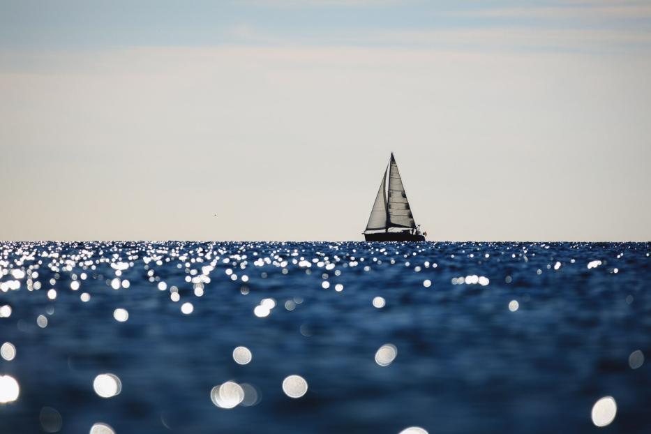 Segelboot auf glitzerndem Meer unter hellem Himmel.