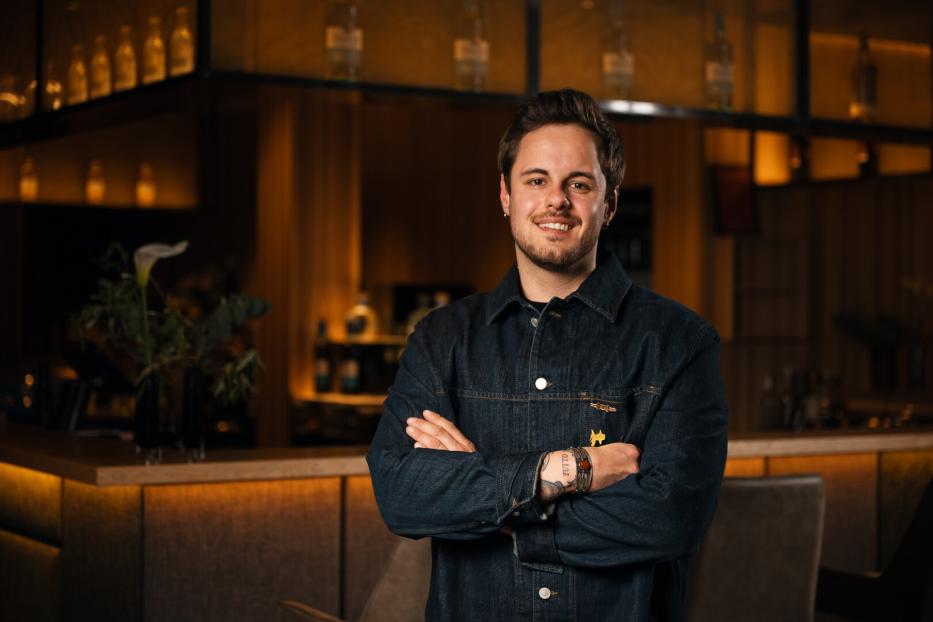 Bartender of the Year 2026 Yannik Seeber steht lächelnd vor einer Bar. 
