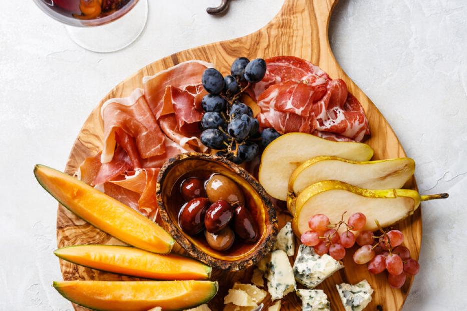 Ein Holzbrett mit Schinken und Käse garniert mit Melone und Birne