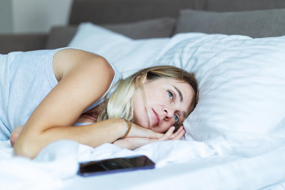 Mid adult woman lying in bed with mobile in depression