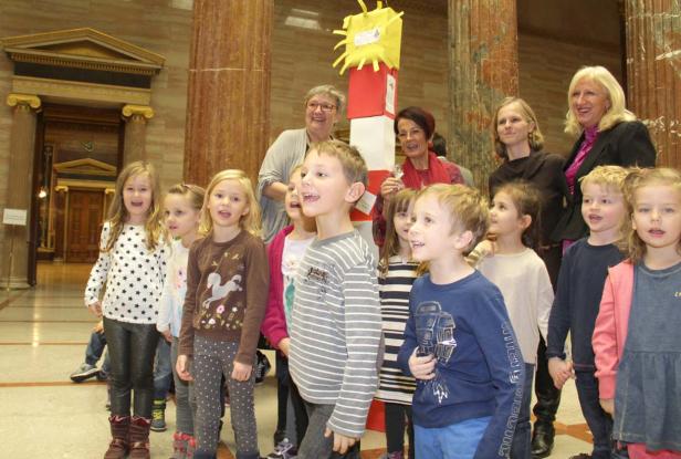 Eine Gruppe von Kindern und Erwachsenen steht in einem Gebäude mit Säulen.