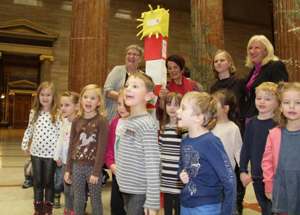 Eine Gruppe von Kindern und Erwachsenen steht vor Säulen in einem Gebäude.