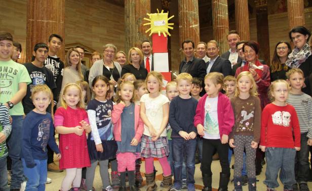 Eine Gruppe von Kindern und Erwachsenen posiert vor einem Leuchtturmmodell in einem Gebäude mit Säulen.