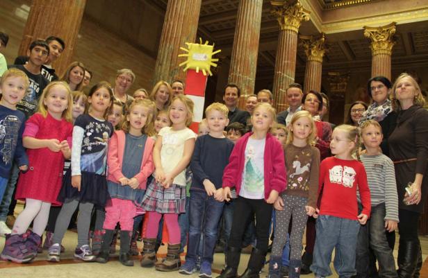 Eine Gruppe von Kindern und Erwachsenen posiert vor Säulen in einem Gebäude.