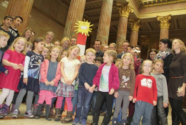 Eine Gruppe von Kindern und Erwachsenen steht in einem Raum mit Säulen.