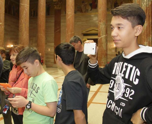 Eine Gruppe von Menschen, die in einem Gebäude mit Säulen ihre Handys benutzen.
