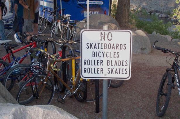 Ein Schild verbietet Skateboards, Fahrräder, Rollerblades und Rollschuhe; Fahrräder stehen davor.