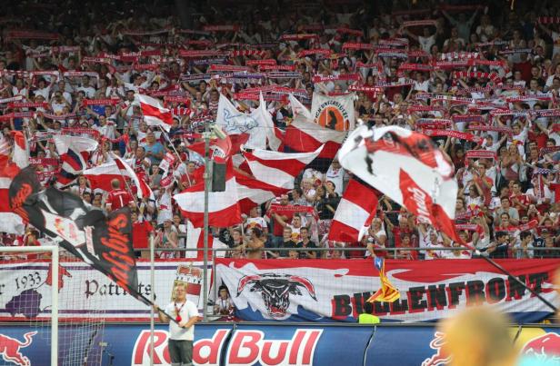 Eine große Menschenmenge feuert ein Fußballteam mit rot-weißen Fahnen und Bannern an.