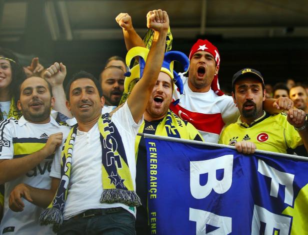 Eine Gruppe Fenerbahçe-Fans jubelt mit erhobenen Fäusten und Vereinsfarben.