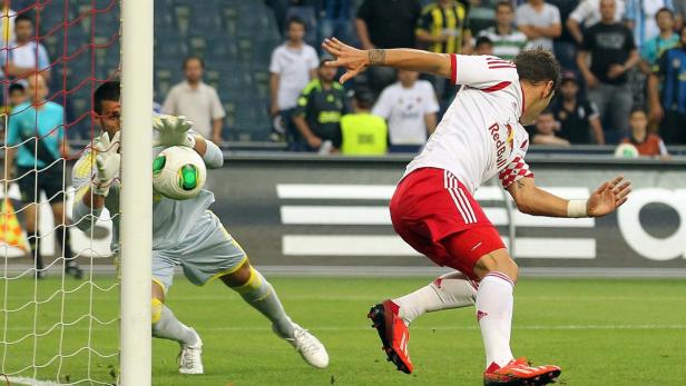 Ein Fußballspieler schießt auf das Tor, während der Torwart versucht, den Ball abzuwehren.