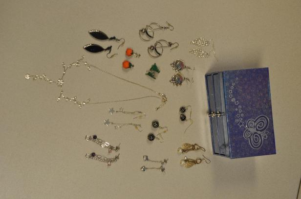 Verschiedene Schmuckstücke, darunter Ohrringe und Halsketten, liegen neben einer blauen Schmuckschatulle.