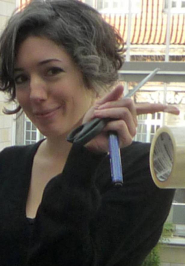 Eine Frau hält eine Schere, einen Stift und eine Rolle Klebeband in der Hand.