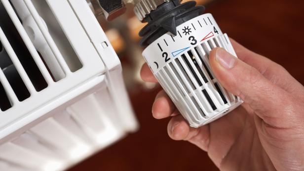 Eine Hand regelt ein Heizkörperthermostat auf Stufe 3.