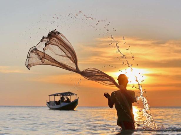Ein Fischer wirft sein Netz im Meer bei Sonnenuntergang aus.