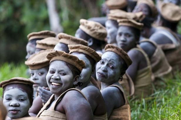 Eine Gruppe Frauen mit bemalten Gesichtern und traditionellen Hüten steht im Gras.
