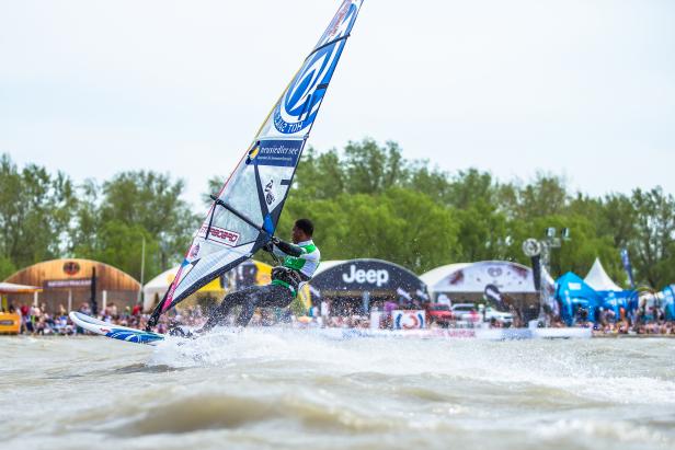 Ein Windsurfer rast mit hohem Tempo über das Wasser.