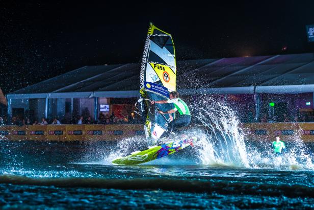 Ein Windsurfer springt bei Nacht mit seinem Board über das Wasser.