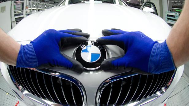 Ein Arbeiter mit Handschuhen montiert das BMW-Logo an einem weißen Auto.