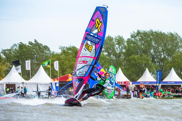 Ein Windsurfer rast mit seinem farbenfrohen Segel über das Wasser in Podersdorf.