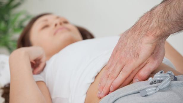 Eine Frau liegt, während ein Arzt ihren Bauch abtastet.