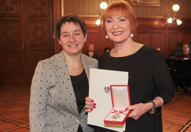 Zwei Frauen posieren mit einem Verdienstorden in einem roten Etui.