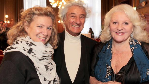 Drei Personen posieren lächelnd für ein Foto in einem eleganten Raum.