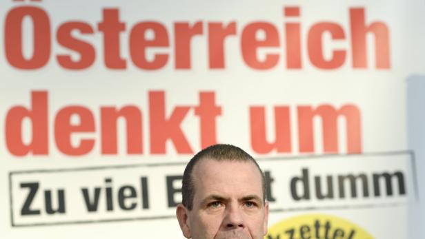 Ein Mann steht vor einem Plakat mit der Aufschrift „Österreich denkt um. Zu viel E ist dumm“.