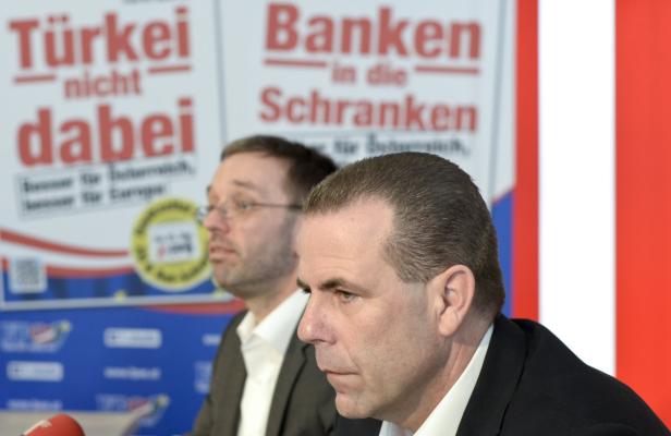 Zwei Männer stehen vor Plakaten mit politischen Botschaften.