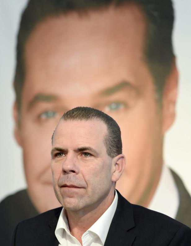 Ein Mann steht vor einem großen Porträt eines anderen Mannes.