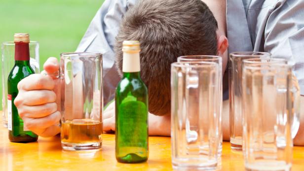 Ein Mann liegt betrunken auf einem Tisch mit leeren Biergläsern und Flaschen.