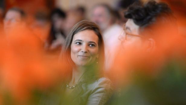 Eine lächelnde Frau mit Perlenkette, gesehen durch unscharfe orangefarbene Elemente.