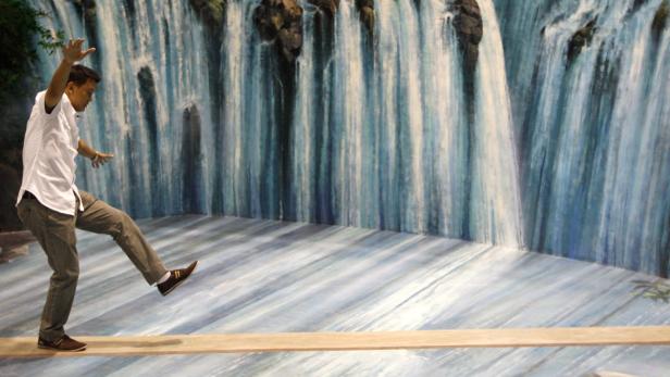 Ein Mann balanciert auf einem Brett vor einem gemalten Wasserfall.