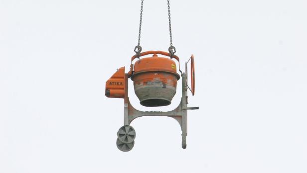 Ein orangefarbener Betonmischer der Marke Atika hängt an Ketten.